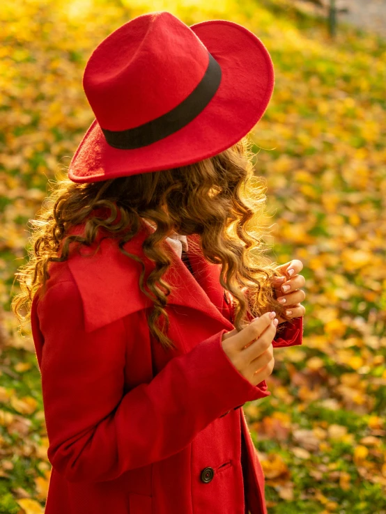 a little girl in a red jacket and hat playing with a yellow leaves