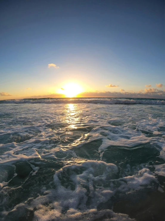 the sunset behind some water waves on the beach