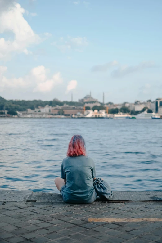 a red haired woman sitting on concrete in front of water