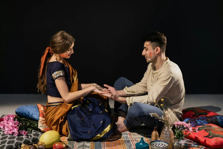 a couple sitting on the ground surrounded by various fabrics and items