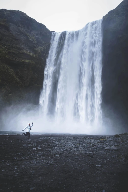 a surfer carries his surfboard under the waterfall