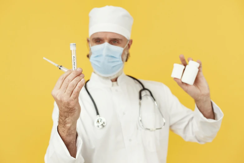 the man is wearing a surgical mask holding two small cigarettes