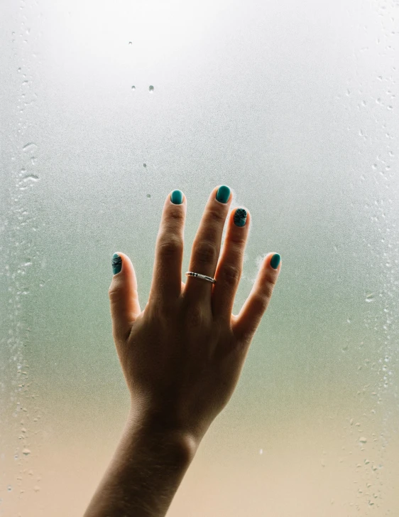 a woman's hand with blue nails is on a window