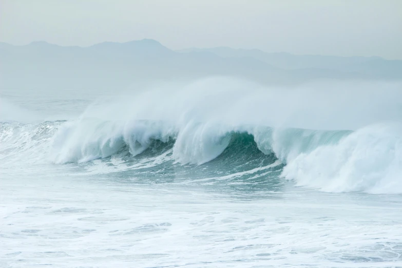 the large wave is in front of a mountain