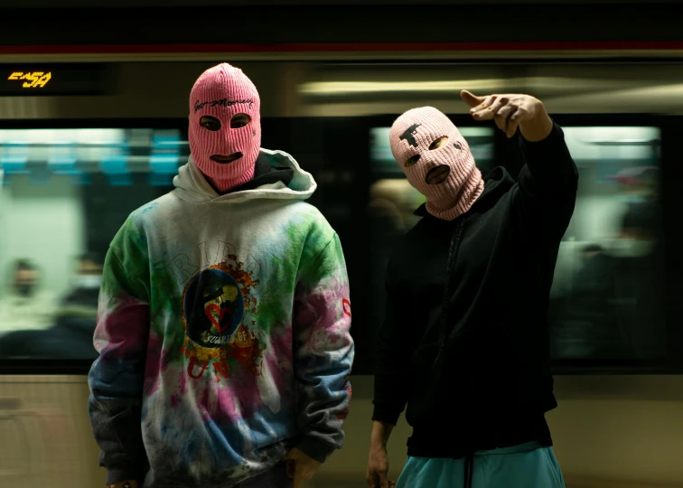 two people with masks standing next to a subway