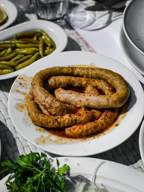 a white plate topped with sausage covered in sauce next to bowls of beans