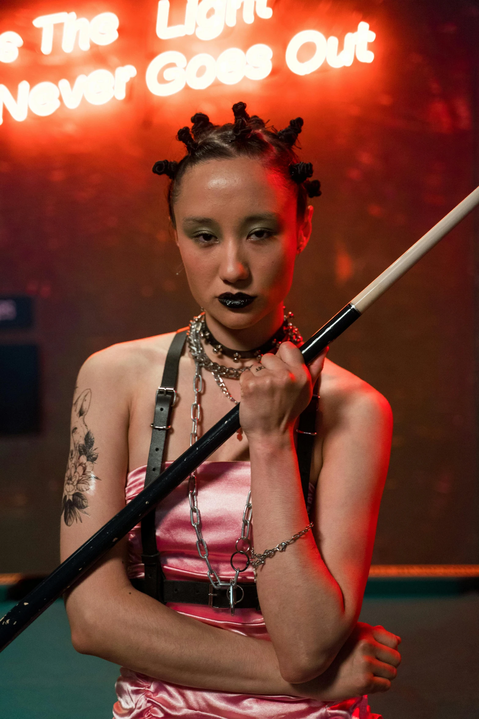 the woman is wearing a halter, choker and belt while she holds a stick