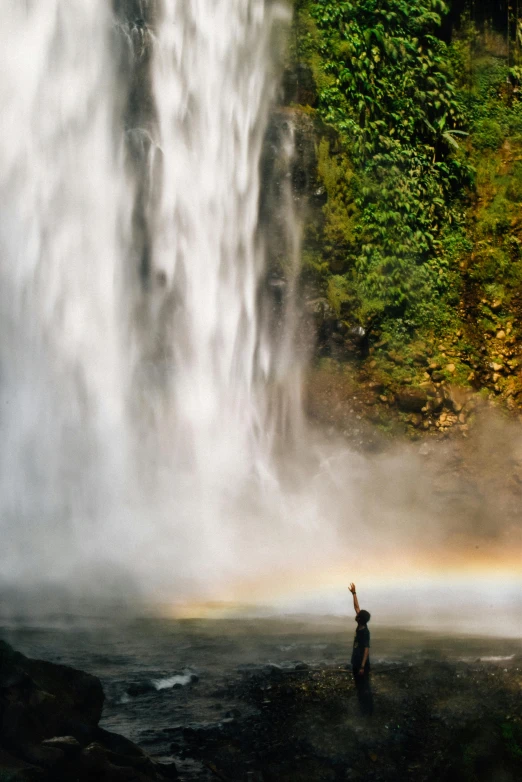 a man stands in front of the water near the waterfall