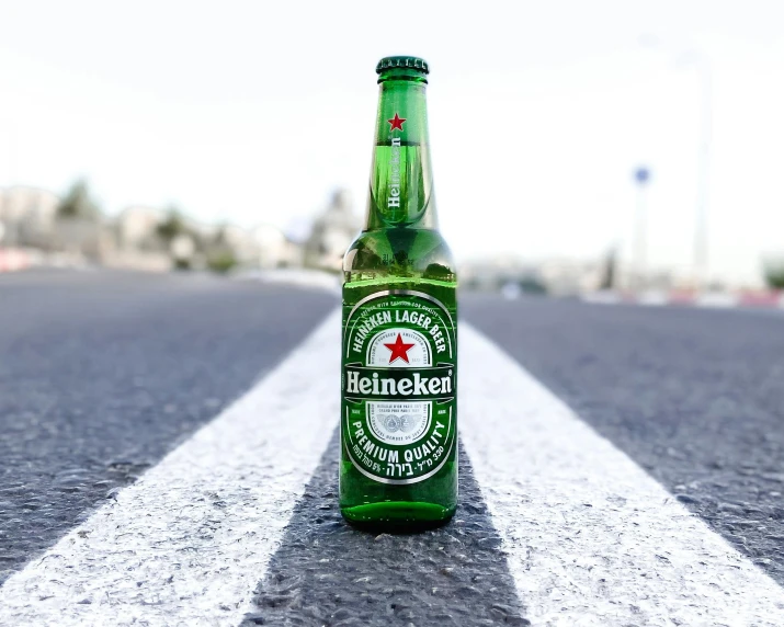 an empty beer bottle sitting on a asphalt road