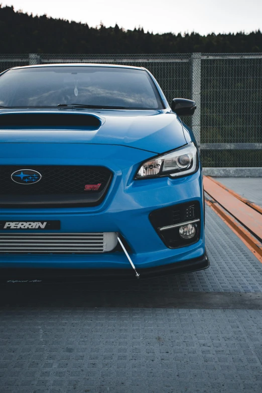 a close up s of the front bumper and headlamp of a blue subaruce on a car