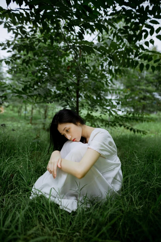 a woman sitting on the grass under a tree