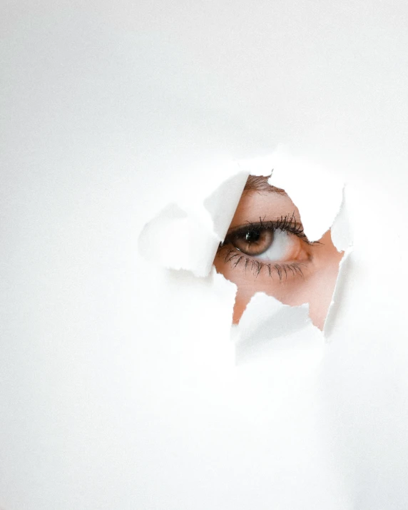 a woman's eye through a hole in white paper