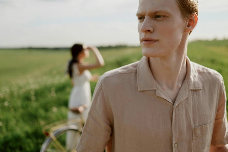 two people stand in a field, one of them on a bike