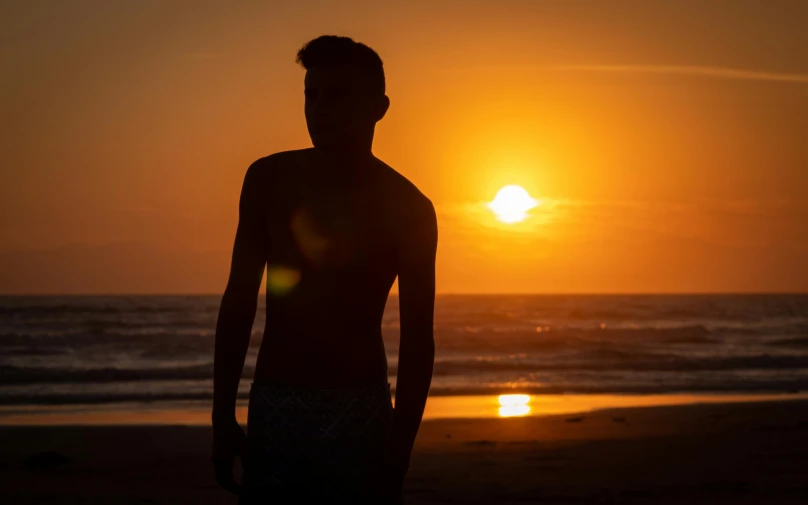 the silhouette of a man standing on the beach at sunset