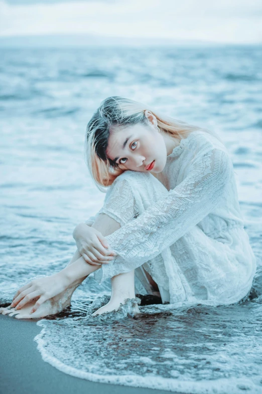 a woman in white clothing sitting on the beach