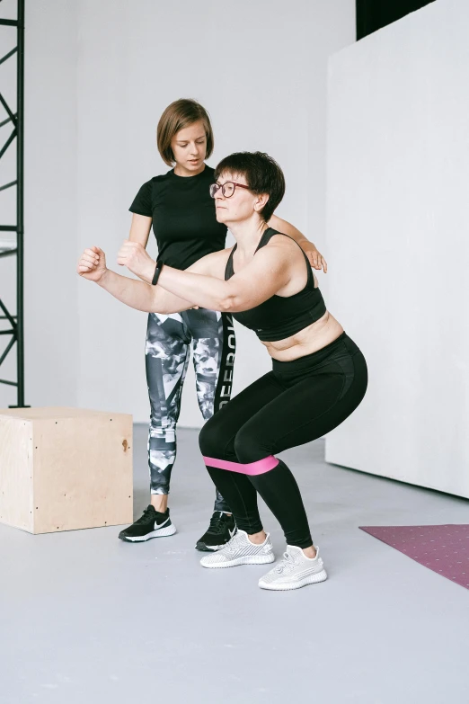 two women in black sports clothes doing squats on a wooden box