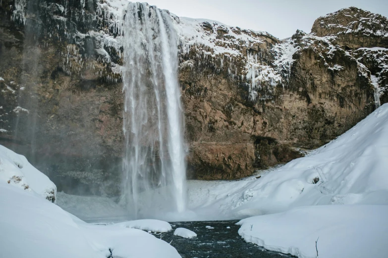 the waterfall is spouting water next to snow covered mountains