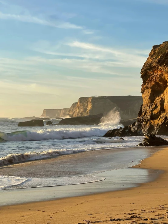 a large rock near the beach has waves coming ashore