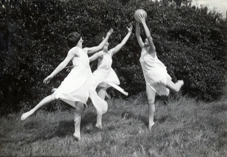 three women in white dresses are playing with a basketball