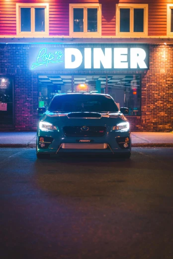 a neon lit diner at night in front of a large brick building