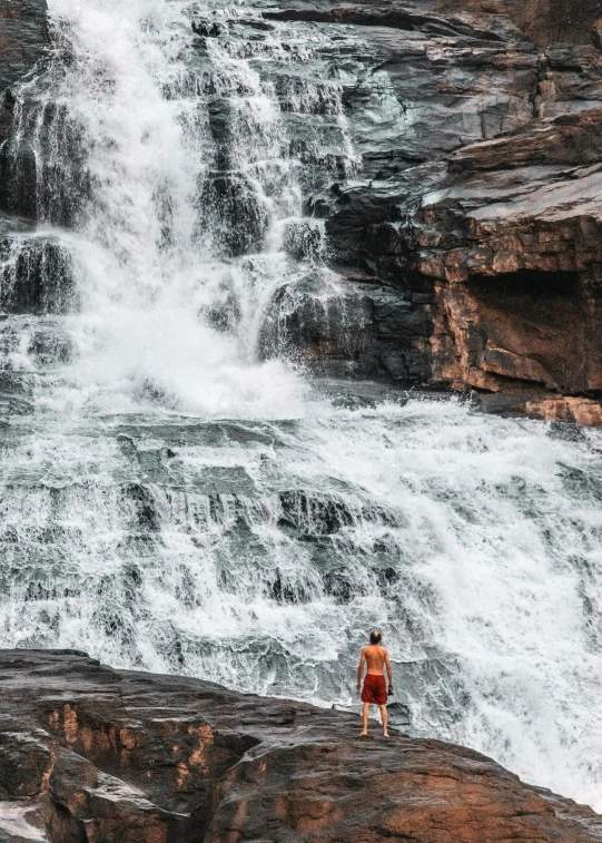 a man is standing on a rock by a waterfall