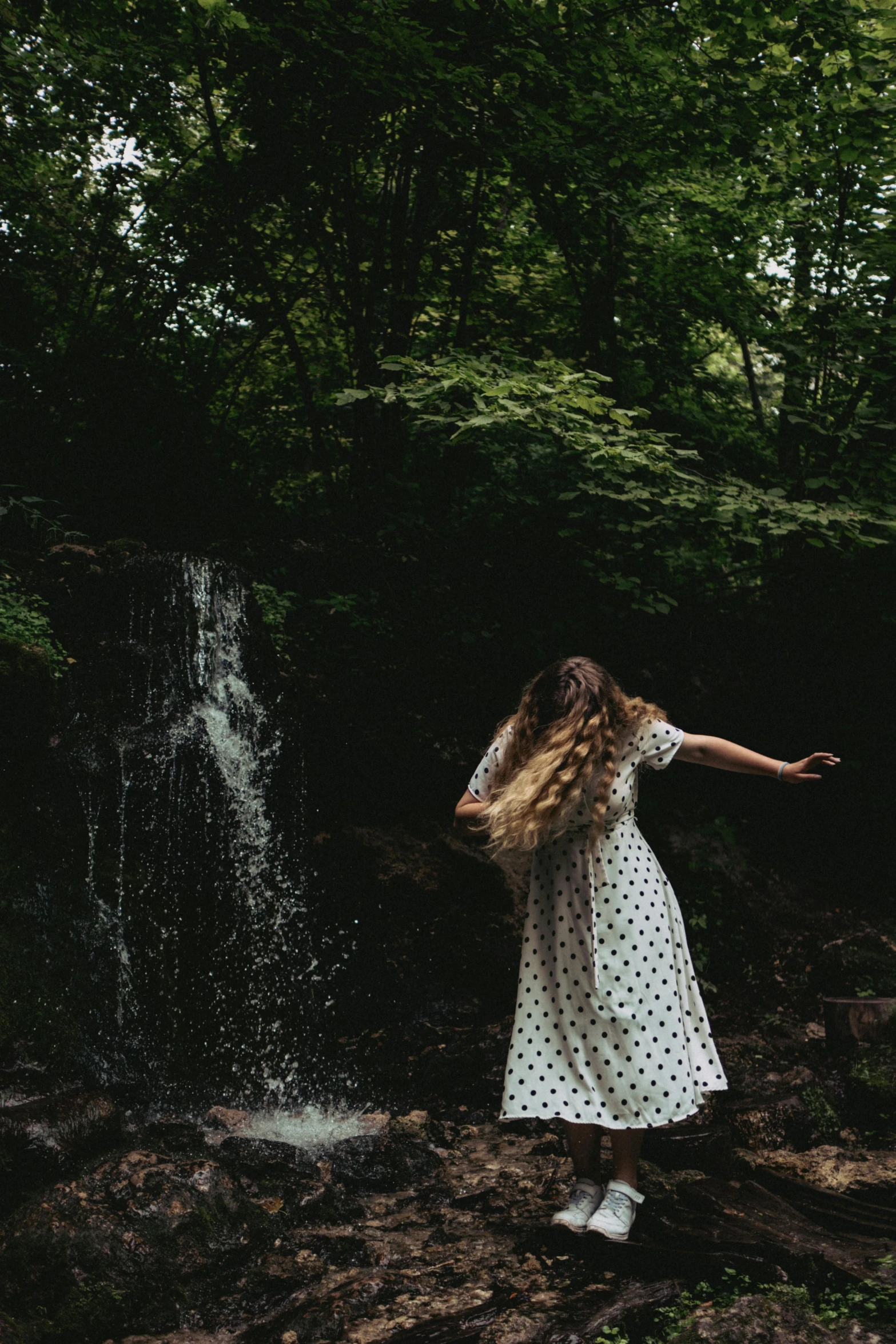 a young woman in polka dots is standing by a waterfall