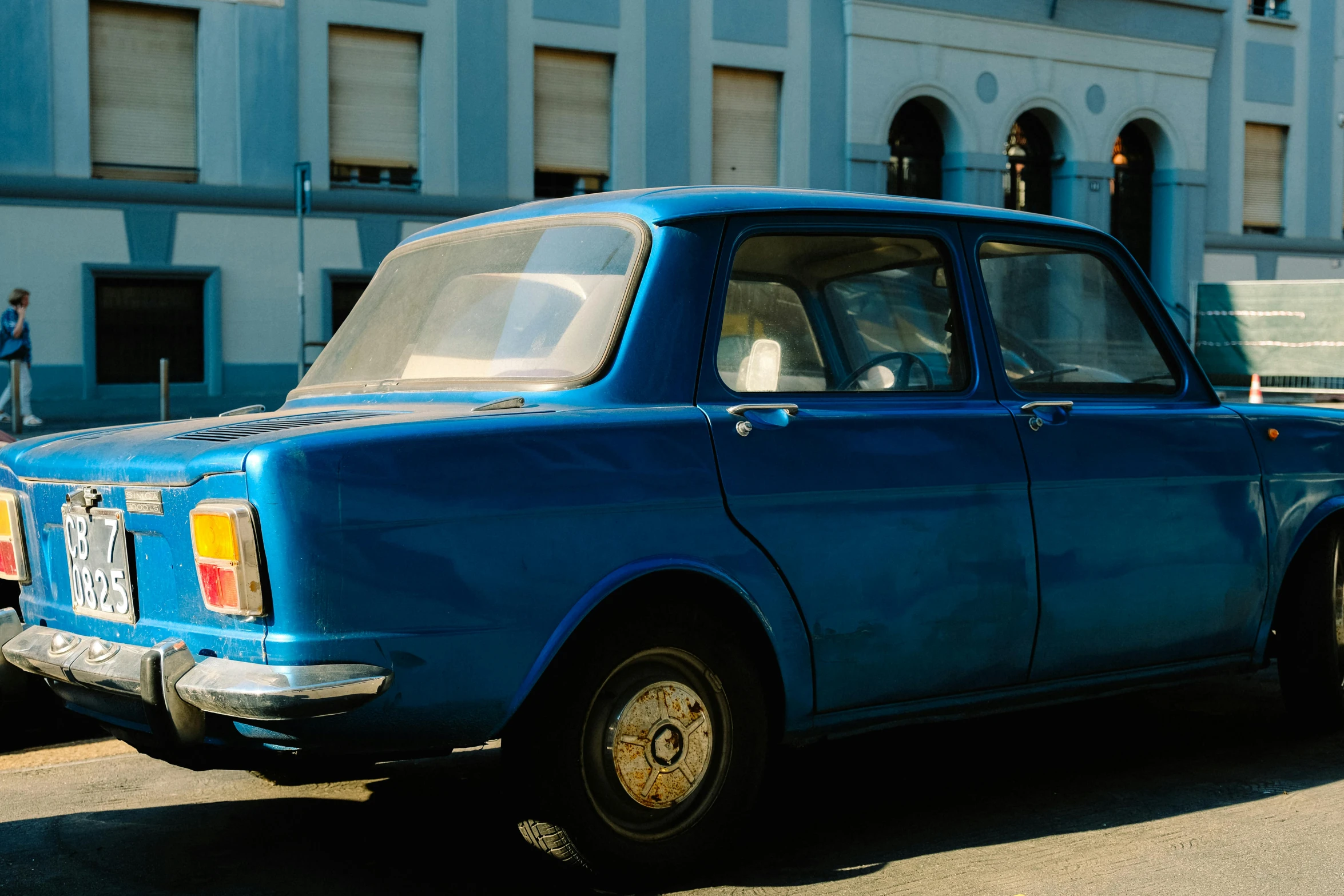 an old, blue car parked by the curb in front of a building