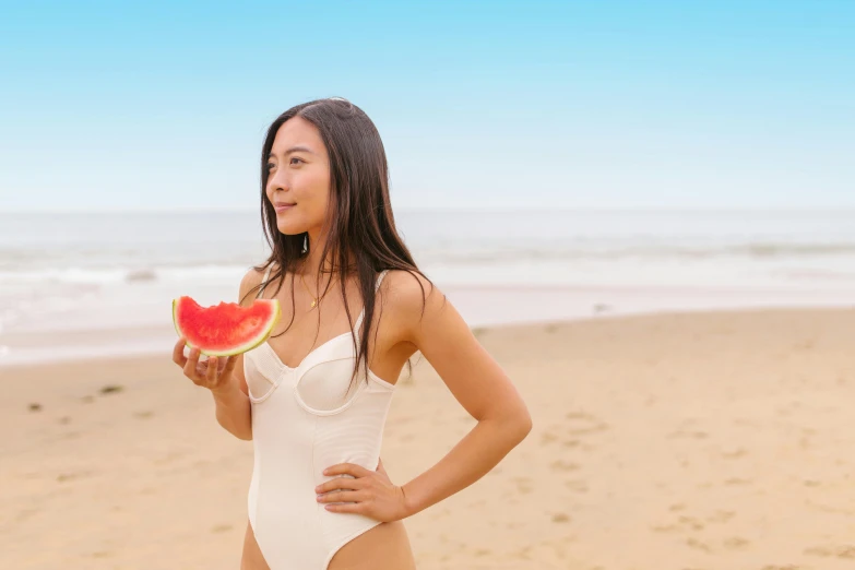 a woman posing on the beach eating watermelon