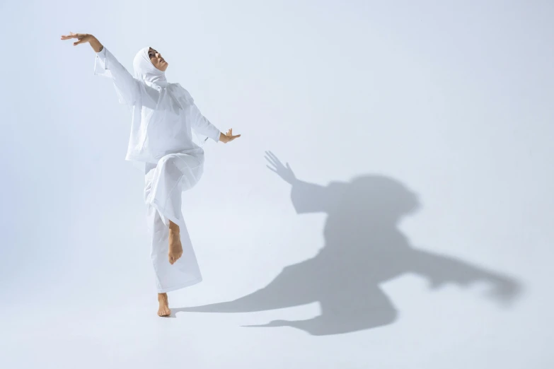 a man in white clothing standing against a wall