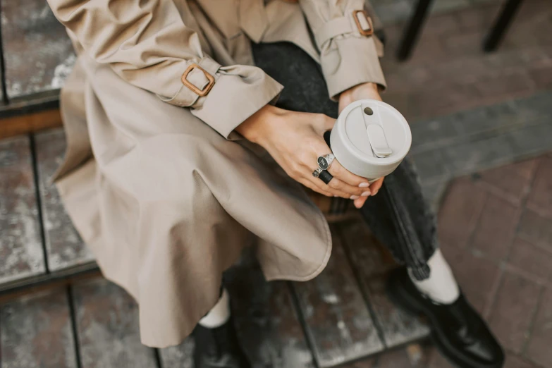 the person in a trench coat has a coffee cup