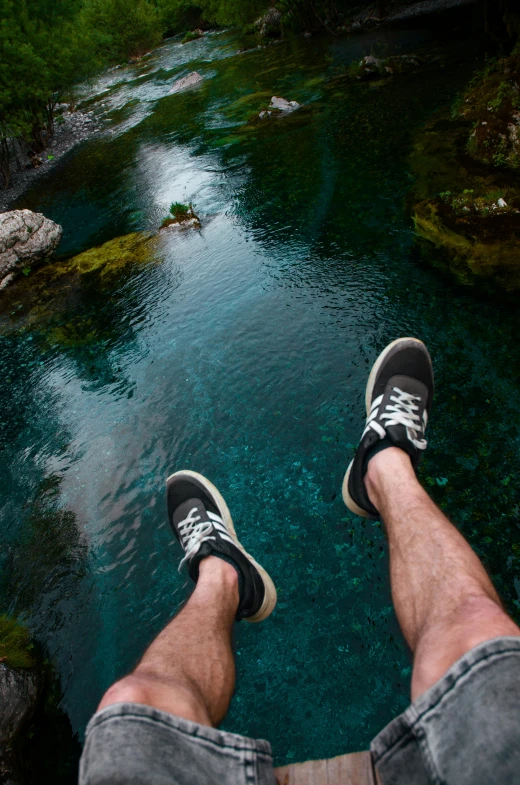 a person wearing shoes standing on a wooden platform looking down at a river