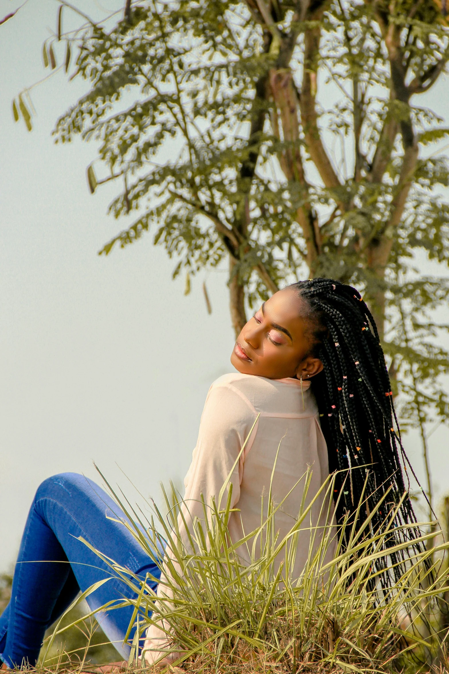 a woman sitting on a hill, wearing jeans and a sweater