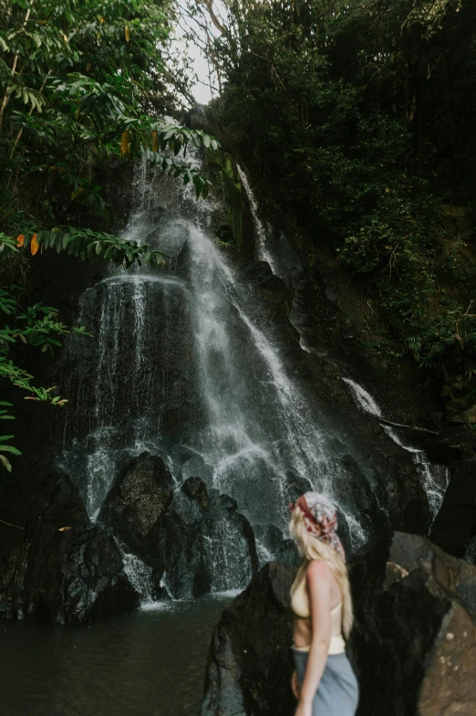 a beautiful blond haired woman standing in front of a waterfall