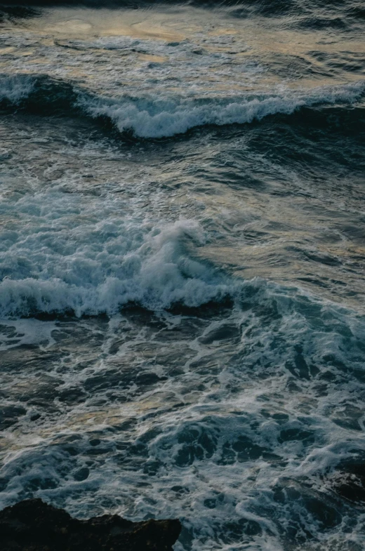 a bird sitting on top of the ocean with waves coming over the rocks