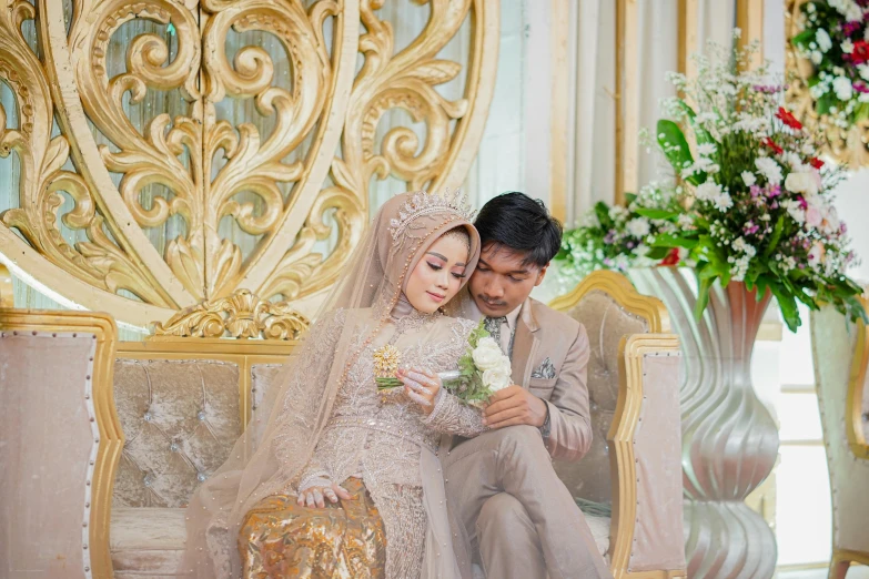 a man and woman in wedding attire sit on a gold couch together