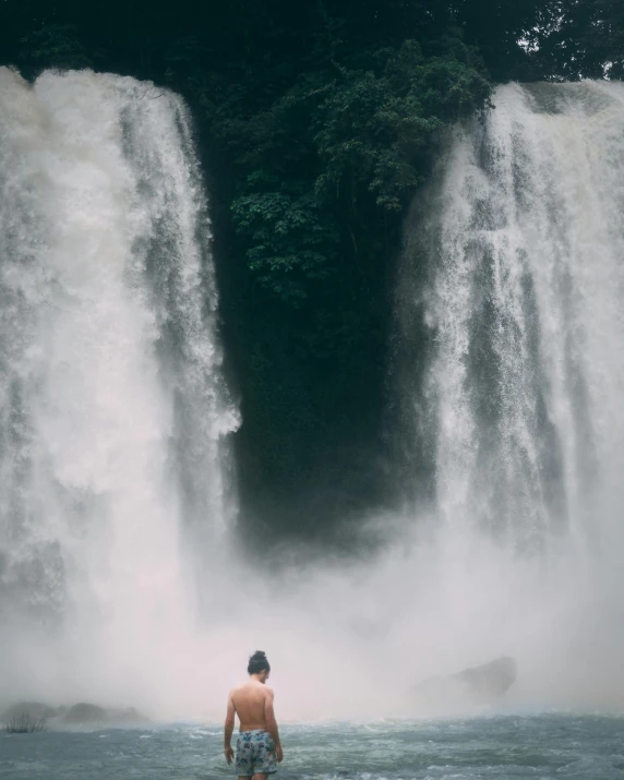 a man standing in the water looking at a large waterfall