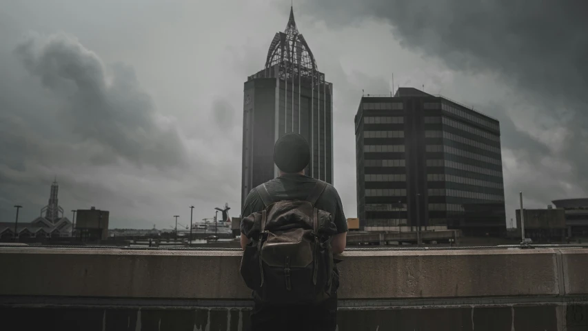 man stands by his back against wall overlooking city