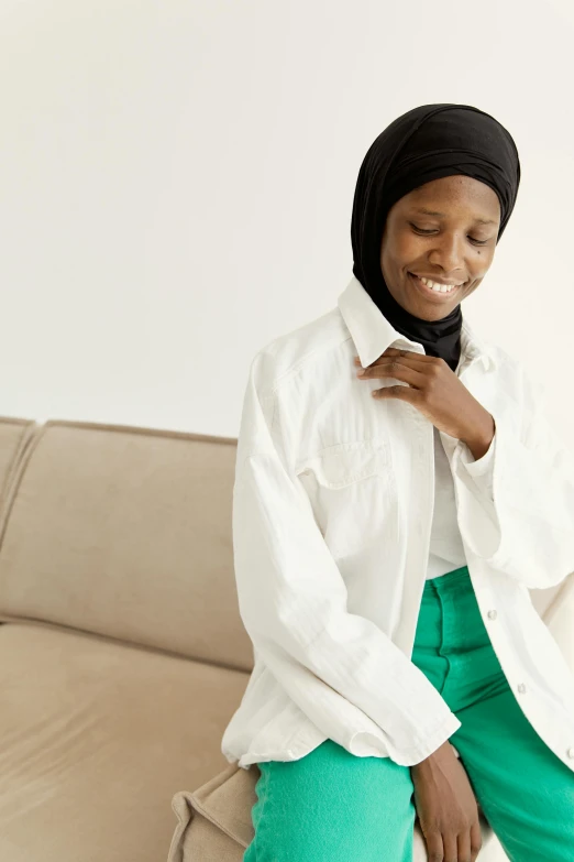 a woman wearing green pants stands against a cream couch