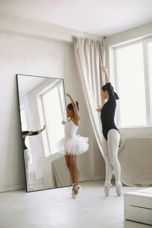 two girls in ballet clothes dance in a white room