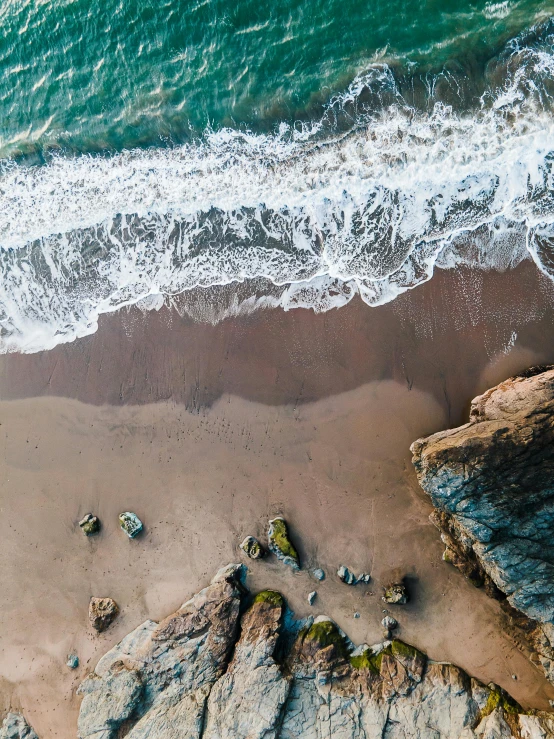 the aerial view of some rocks and water near a beach