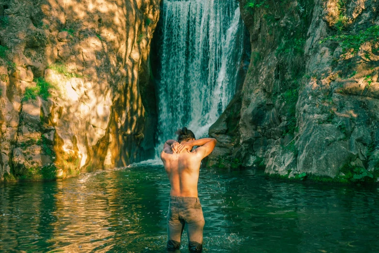 a man wading in a river next to a waterfall