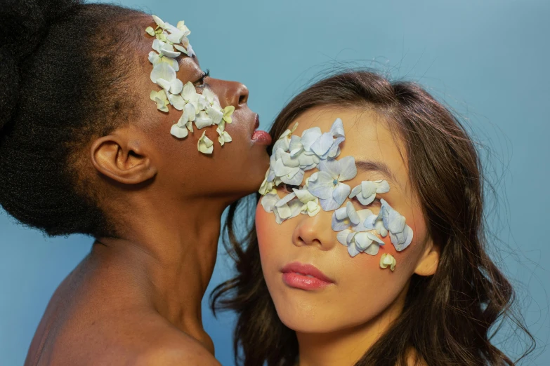 two beautiful woman kiss each other and have their faces decorated with flowers