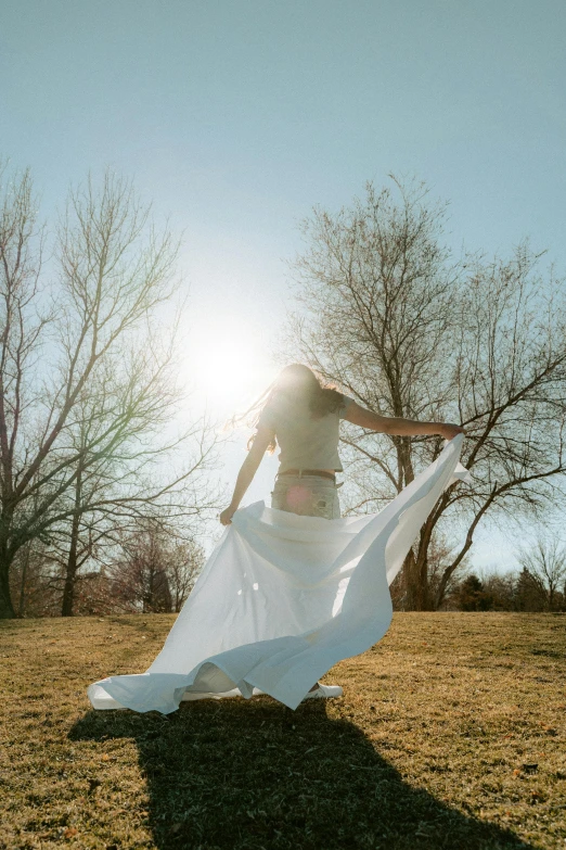 a young woman standing in a field with her white fabric blowing in the wind