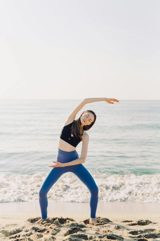 a woman practices yoga on the beach with her hand in the air