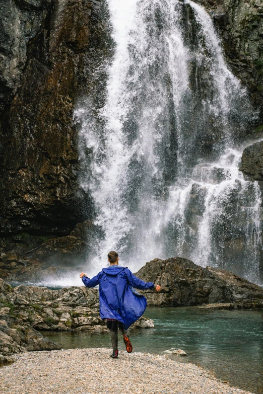 a person in blue coat standing in front of a waterfall