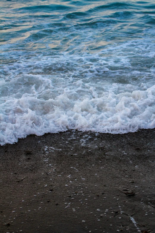 water waves crashing onto a beach area on a cloudy day