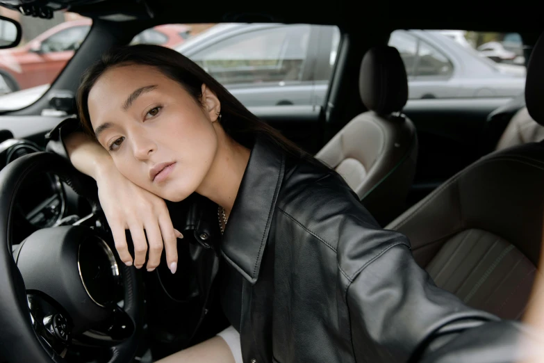 a beautiful young lady in a leather jacket sitting inside a car