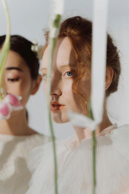 two women, one with red hair, are looking in the mirror