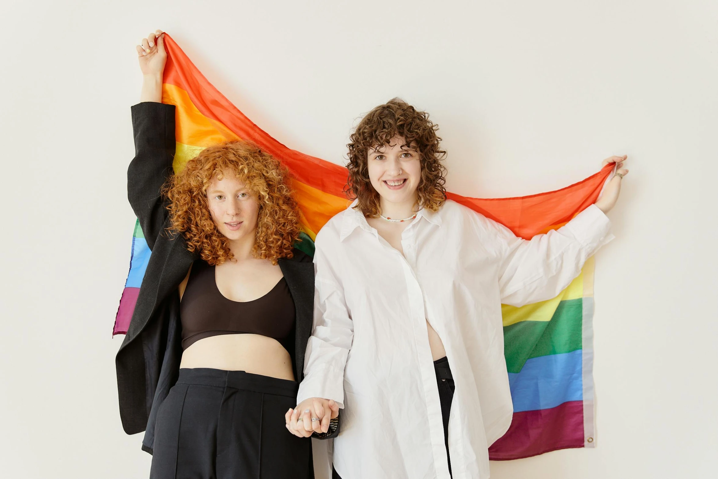 two women wearing black pants, a white shirt and a rainbow flag