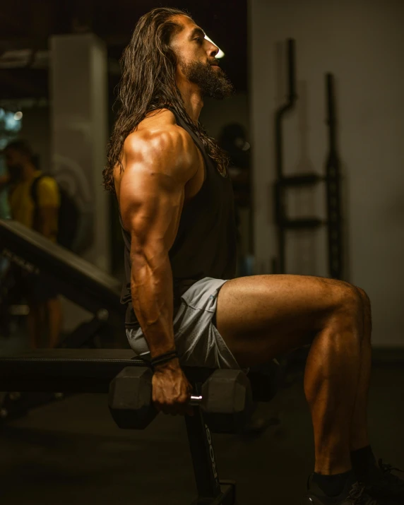 man with long, thick hair is squating on the bench